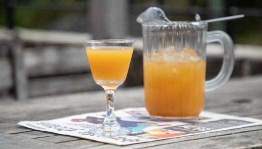 A close up of Bermuda Rum Swizzle with a pitcher and glass on top of a newspaper.
