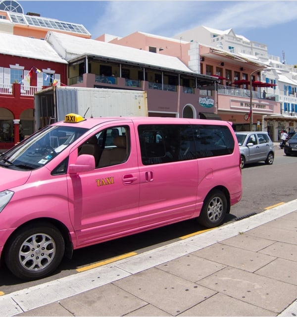 A pink taxi van parked on the side of a road.