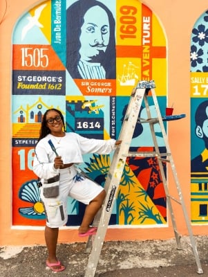 A woman is smiling at the camera with paint brushes.